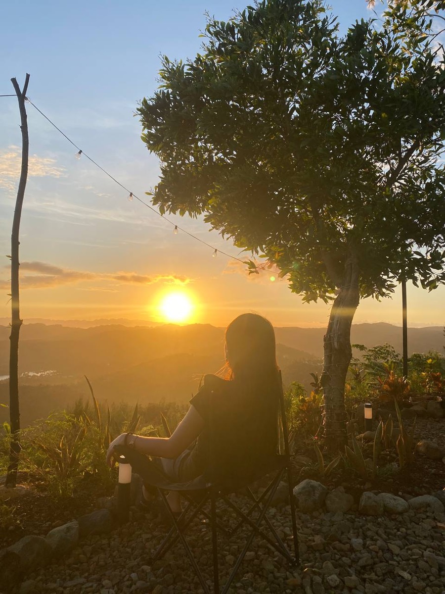 A guest sitting under the tree at Laaganan, watching the sun go down over the hills